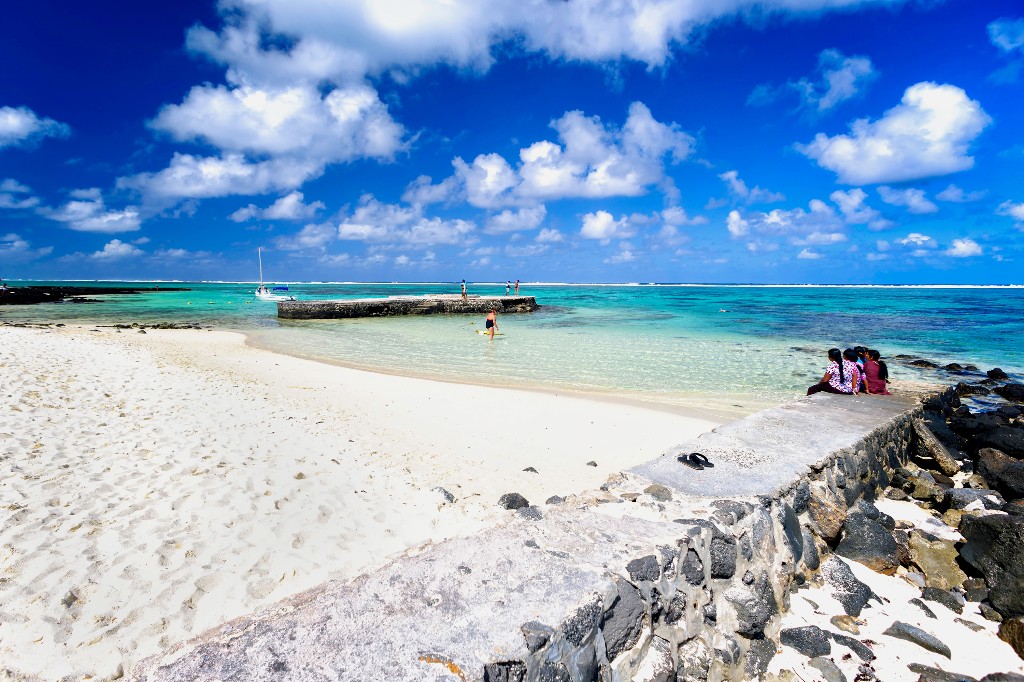 Beachgoers sit on a rock wall on Blue Bay Beach in Mauritius. Image: Leslie Othen, Alamy Stock Photo