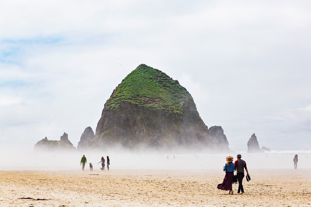 Mist fills Cannon Beach, Oregon, but that does not stop visitors from enjoying a walk. Image: Massimo Colombo, Getty Images