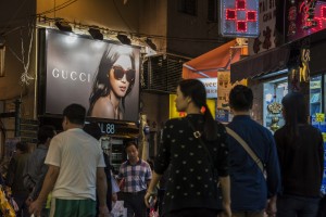 Pedestrians walk past a billboard advertisement for luxury brand Gucci, a unit of Kering SA, in Macau, China, on Tuesday, Dec. 1, 2015. Macau's casino revenue fell for the 18th straight month in November, as China's moves to curb illicit money flows from the mainland deterred the high-stakes players who rely on junket promoters for betting loans. Photographer: David Paul Morris/Bloomberg via Getty Images