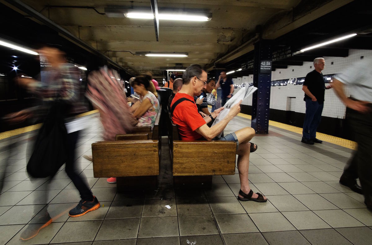 A commuter (R) reads a newspaper as he waits for a train in a subway station in New York on July 1, 2015. Photo credit should read JEWEL SAMAD/AFP/Getty Images