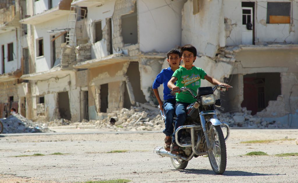 Boys ride a motorcycle near a damaged building during the third day of Eid al-Adha in the rebel controlled city of Idlib, Syria September 14, 2016. REUTERS/Ammar Abdullah