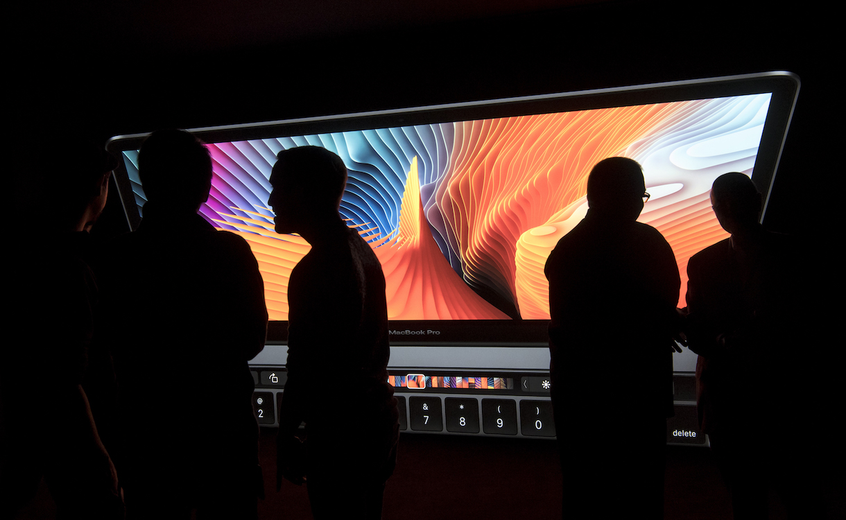 The silhouettes of attendees are seen in front of a display featuring the new MacBook Pro laptop computer during an event at Apple Inc. headquarters in Cupertino, California, U.S., on Thursday, Oct. 27, 2016. Apple Inc. introduced the first overhaul of its MacBook Pro laptop in more than four years, demonstrating dedication to a product that represents a small percentage of revenue. Photographer: David Paul Morris/Bloomberg via Getty Images