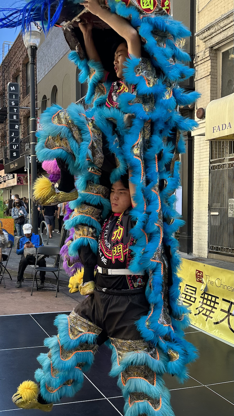 Two Lion Dancers in blue suit, one on the shoulders of the other. 