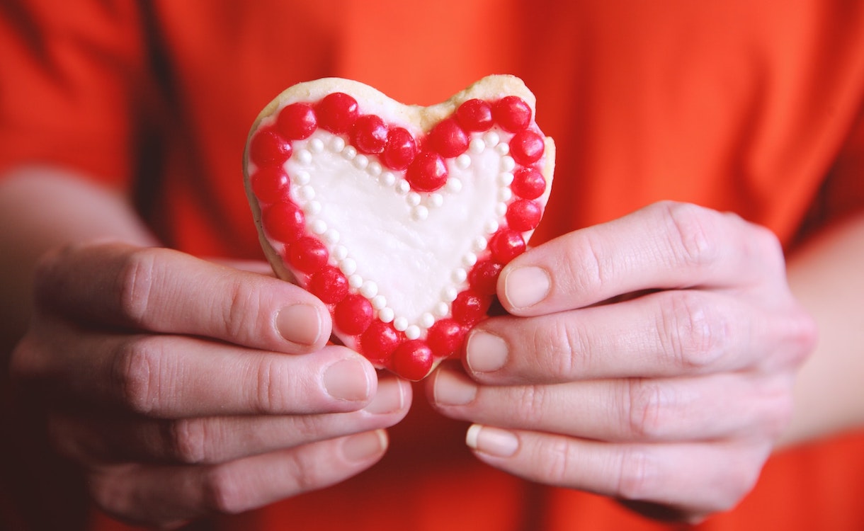 Two hands holding a heart-shaped sugar cookie 